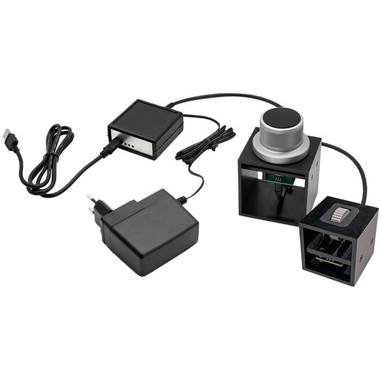 The image shows a HAPTICORE Eval Kit Combi Bundle consisting of a HAPTICORE 14-P001X1 and HAPTICORE 40-P001X1 Eval Kit as well as a HAPTICORE Control Unit Pro, including a 12 V power supply and USB-C connection cable.